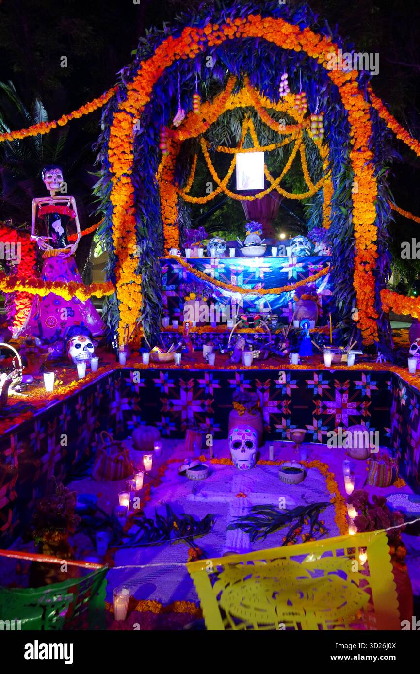 Colorful illuminated Day of the Dead altar decorated with marigold flowers, candles, skeletons, and traditional offerings at night Stock Photo