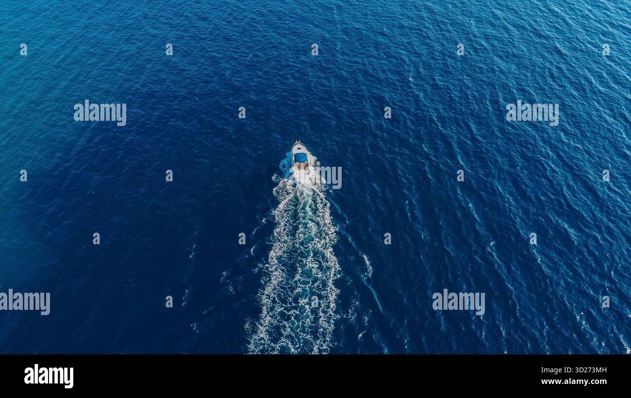 Powerful boat tracing a path of white foam across the vast, deep blue sea, its wake a fleeting signature on the water's surface. Stock Photo