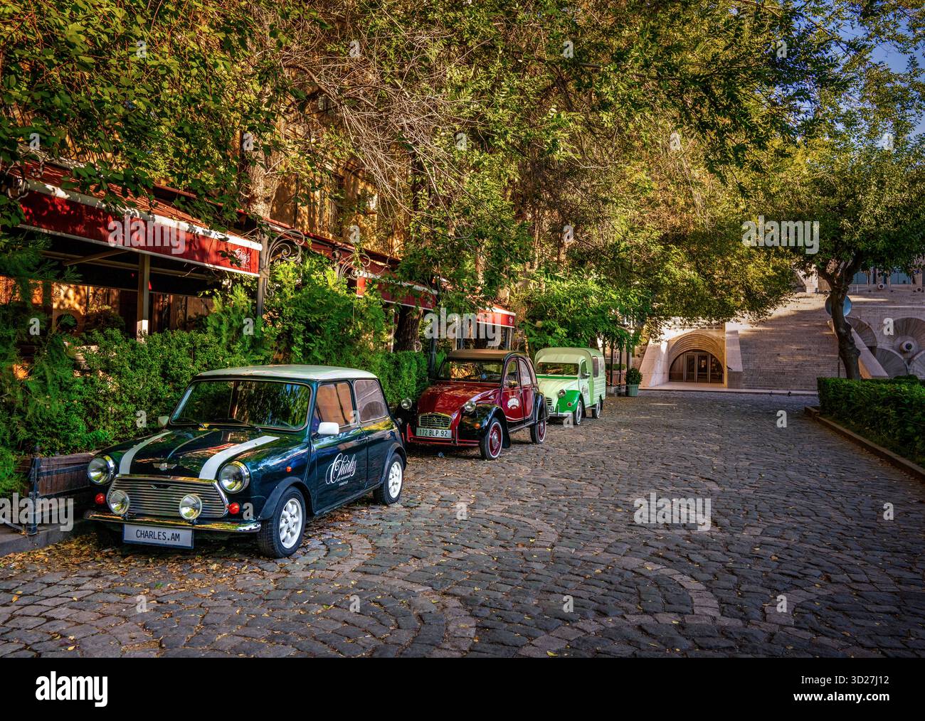 Three vintage cars are parked on a cobblestone street in front of a ...