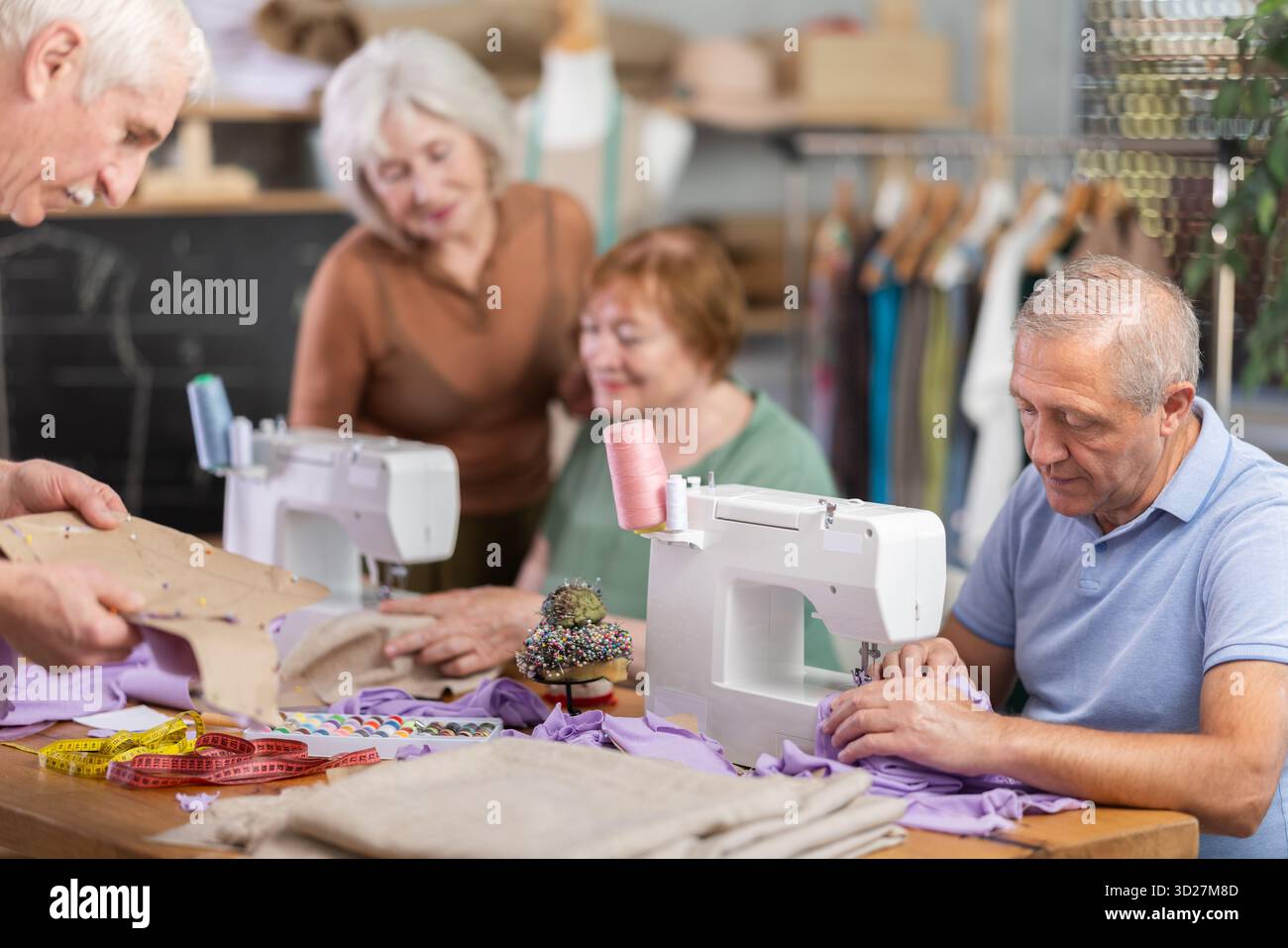 Some people communicate and discuss pattern, while others sew using sewing machine at lesson Stock Photo