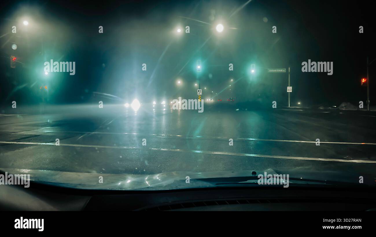 Road intersection at rainy night as seen from a car driver's point of view Stock Photo