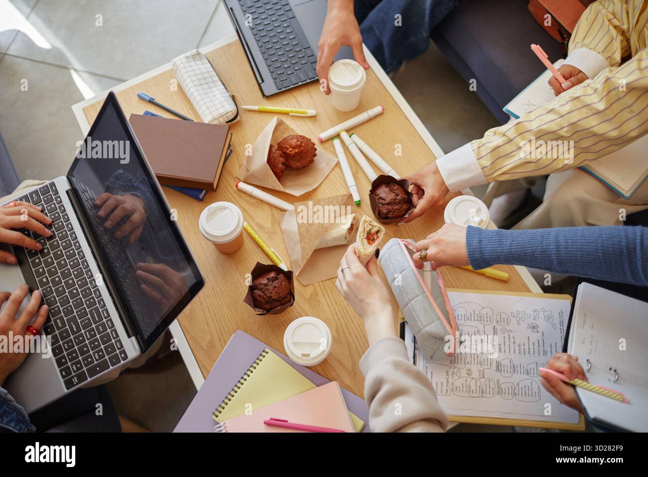 Diverse Young Adults Collaborating on Project While Sharing Snacks and Coffee Stock Photo