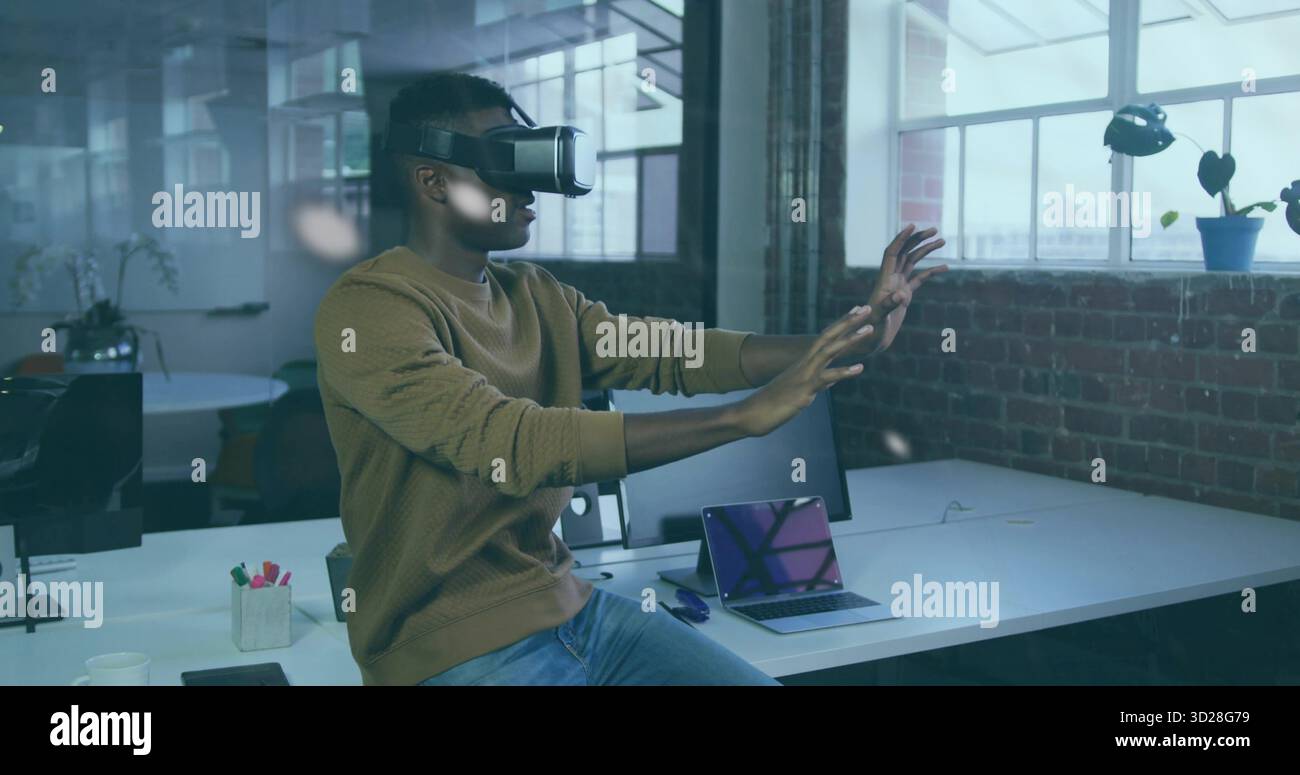 Developer wearing VR headset manipulating virtual interface in office space, with laptop smartphone Stock Photo