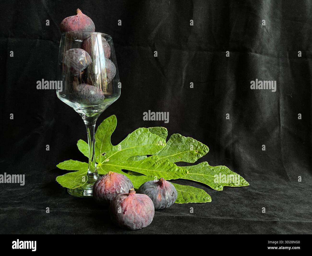 Fresh figs on a black background, served in a glass with two green fig leaves - Smartphone Captured Stock Image