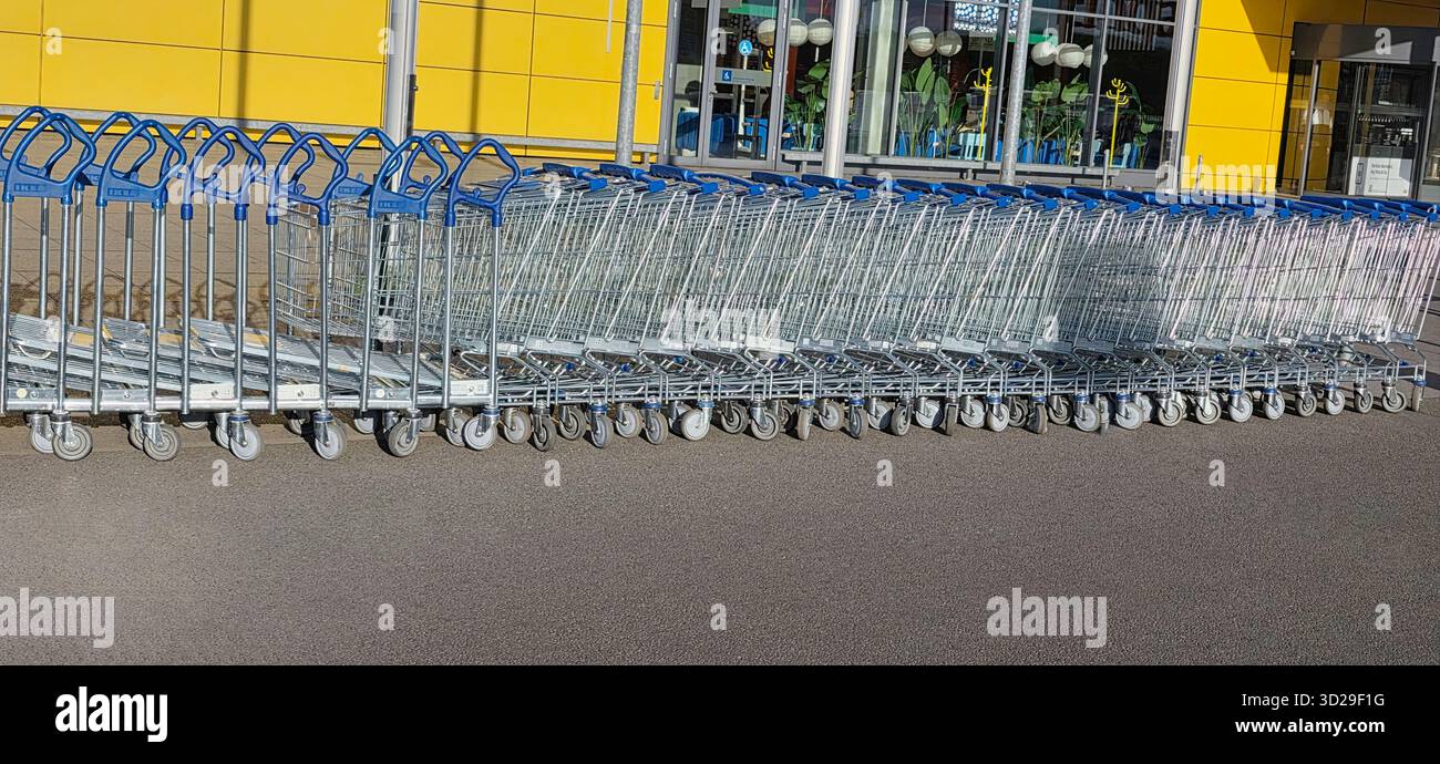 Berlin, Germany - May 05, 2025: Row of metallic shopping carts arranged neatly outside a vibrant yellow store. - Smartphone Captured Stock Image