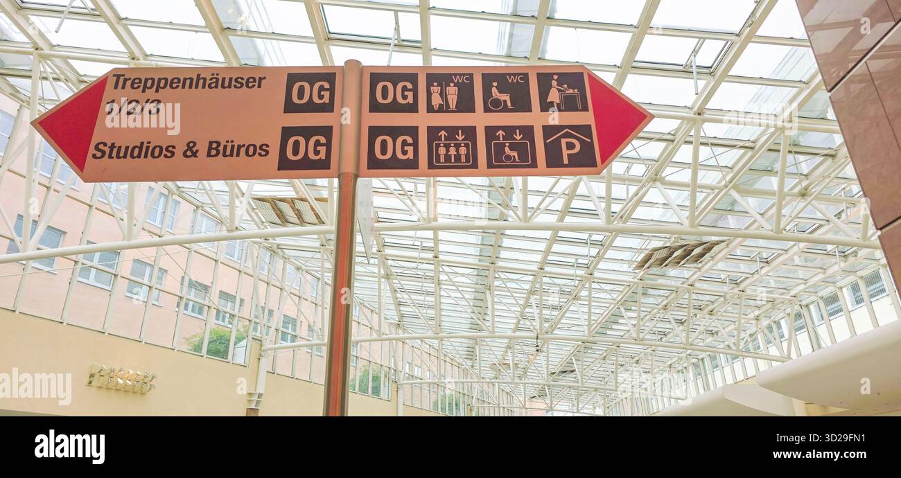 Belin, Germany - May 19, 2025: Directional sign shows various facilities in a modern building with glass ceiling. - Smartphone Captured Stock Image
