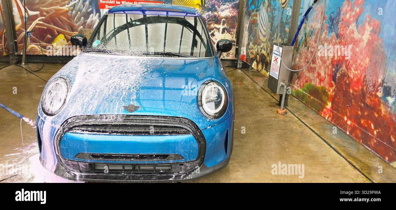 Berlin, Germany - May 18, 2025: Blue Mini Cooper is being washed in an automatic car wash facility with vibrant background. - Smartphone Captured Stock Image