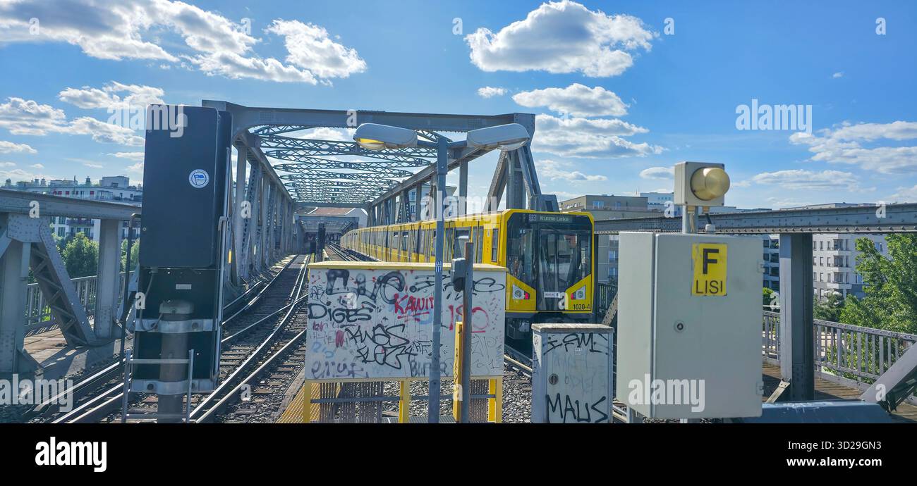 Berlin, Germany - July 04, 2025: Yellow train travels over bridge in urban setting with blue sky and clouds creating a vibrant atmosphere. - Smartphone Captured Stock Image
