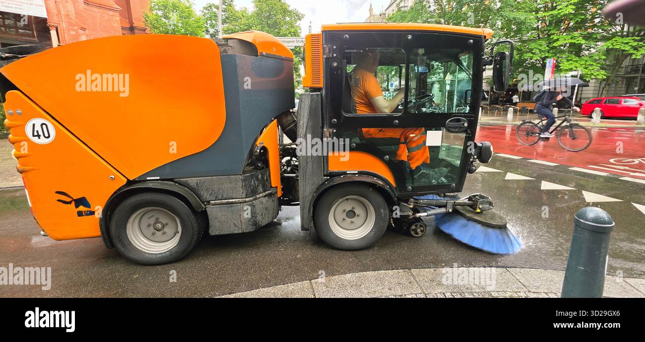 Berlin, Germany - June 05, 2025: Street cleaning machine is actively cleaning urban street with cyclist passing by. - Smartphone Captured Stock Image