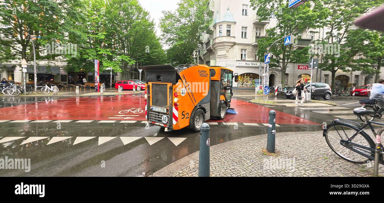 Berlin, Germany - June 05, 2025: Orange street cleaning vehicle is parked on urban street surrounded by trees and buildings. - Smartphone Captured Stock Image
