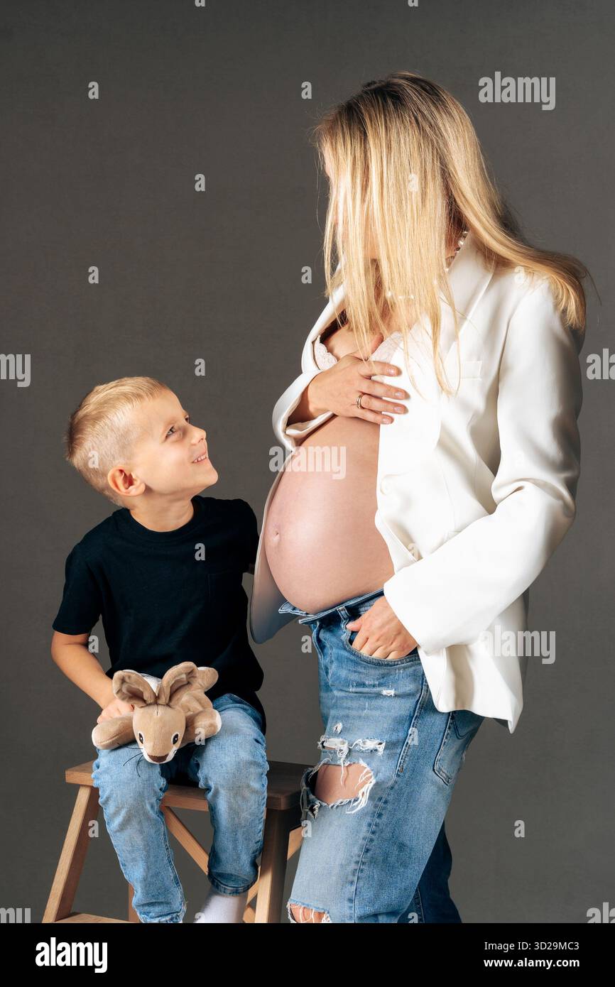 Expecting mother in white blazer with child sitting on stool, modern