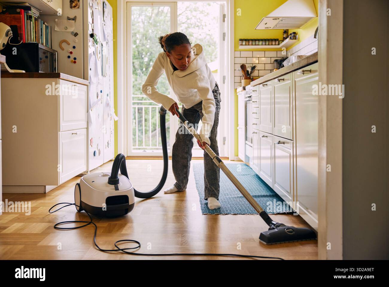 Girl cleaning kitchen floor with vacuum cleaner at home Stock Photo
