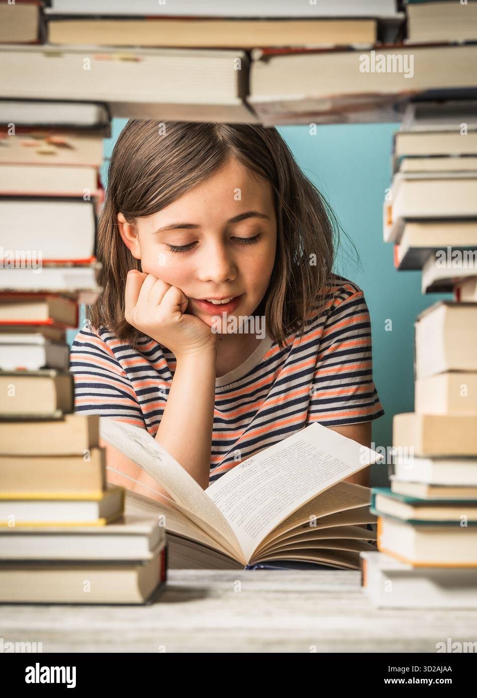 Child girl reads a book with a pile of books beside her Stock Photo - Alamy