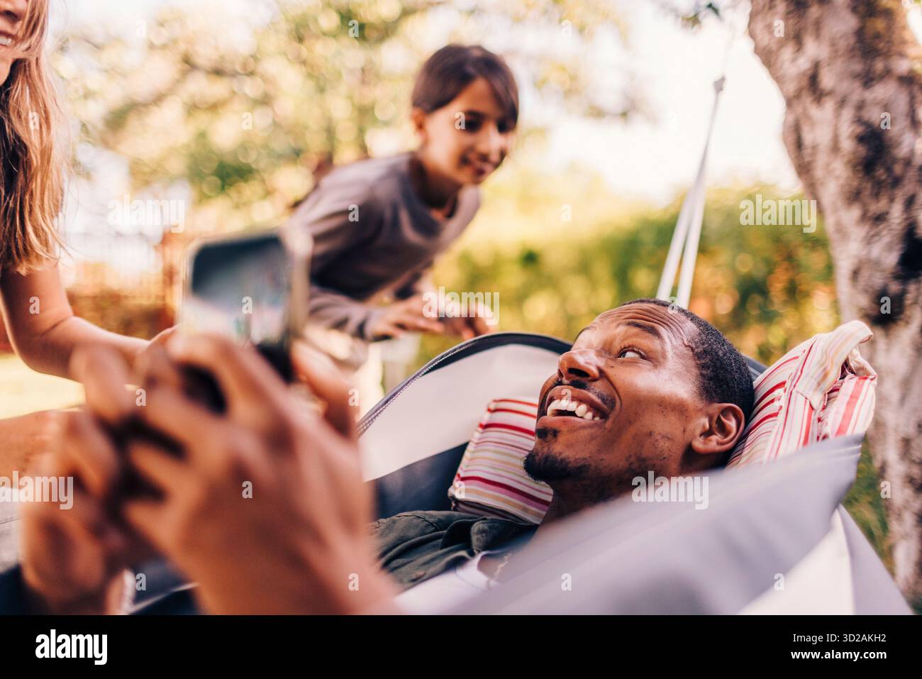 Daughters playing with father lying on hammock Stock Photo