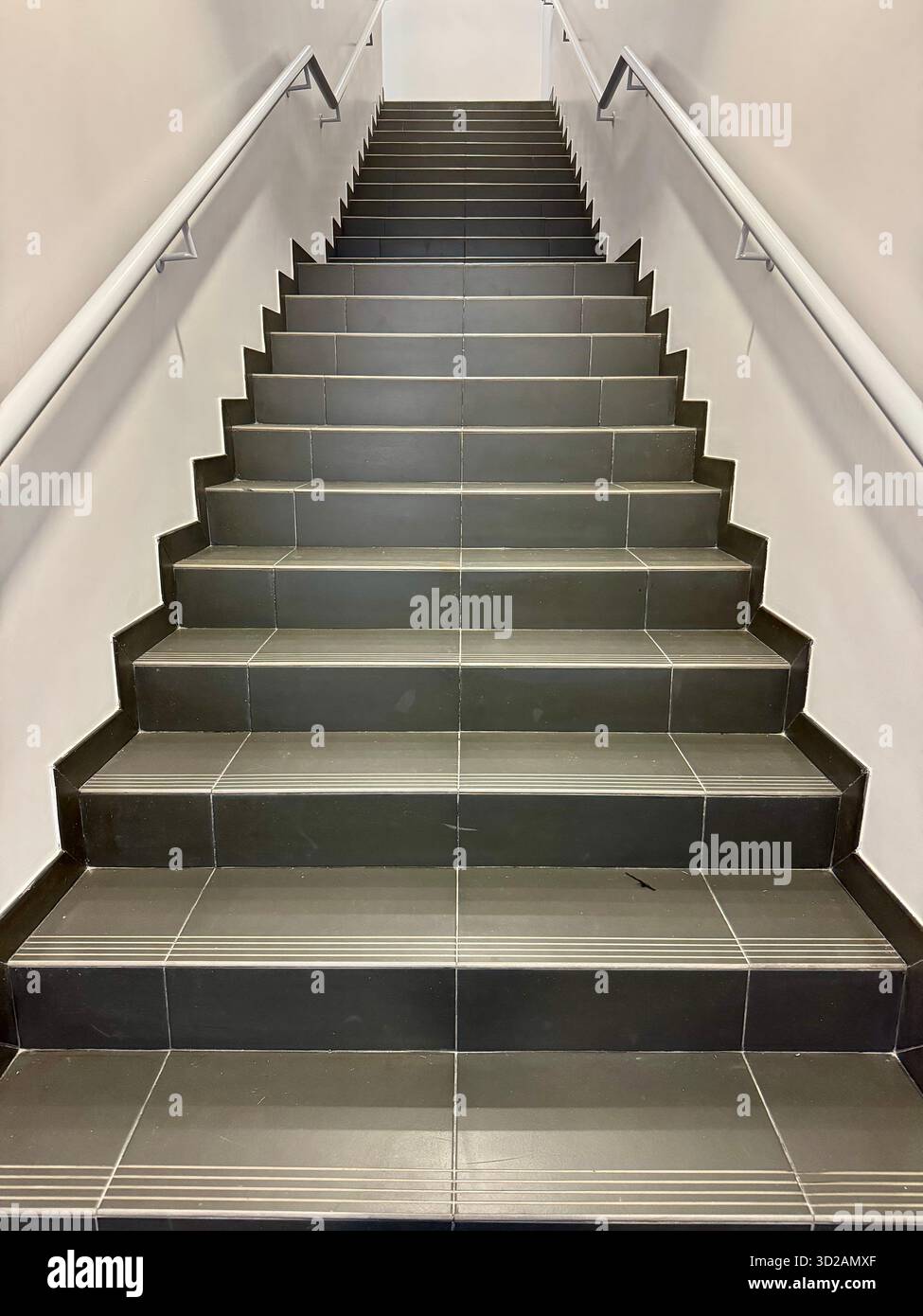 Modern indoor staircase with gray ceramic tiles and white handrails viewed from the bottom looking upward. - Smartphone Captured Stock Image