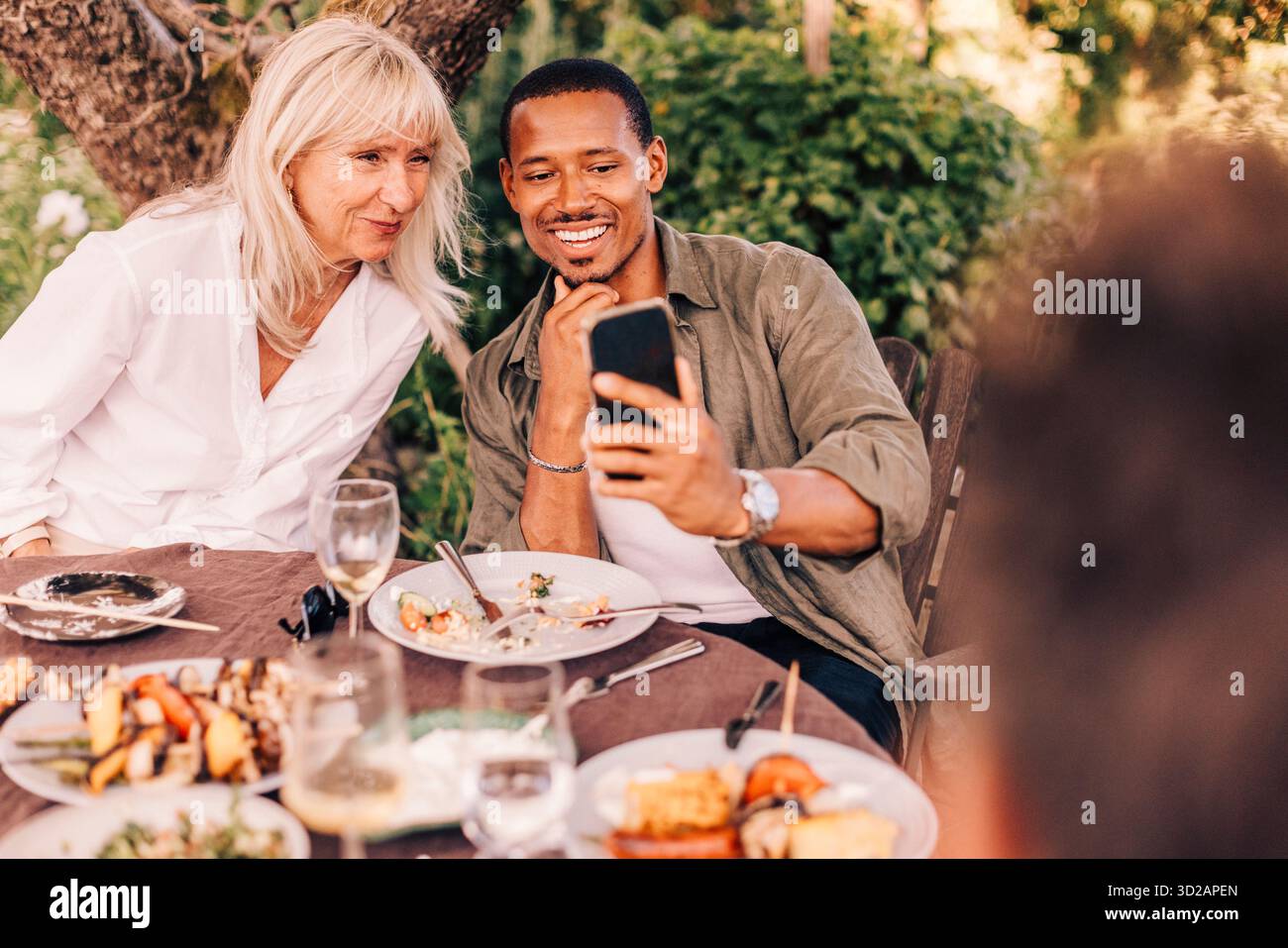 Smiling man taking selfie with mother while sitting at dining table in back yard Stock Photo