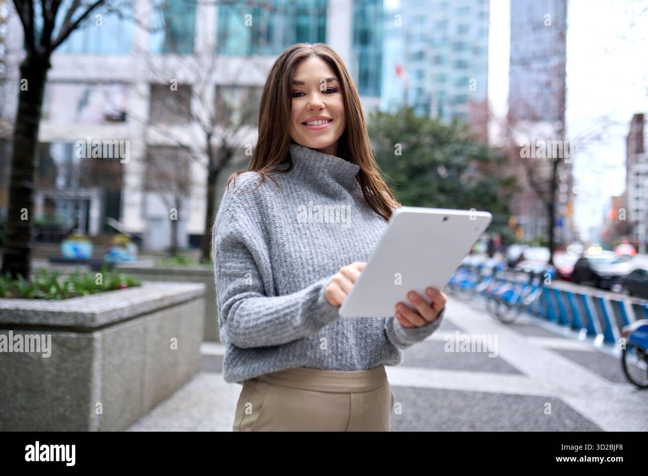 Young happy busy business woman standing in city using digital tablet. Stock Photo