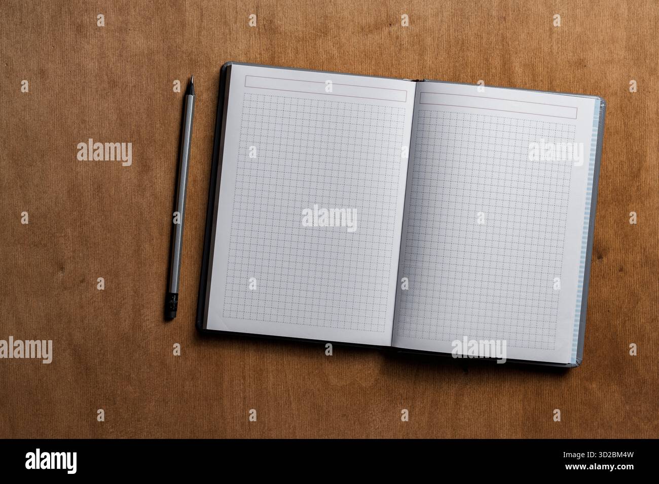 Open notebook with checkered sheets and pencil on wooden texture background, close up, top view, copy space Stock Photo