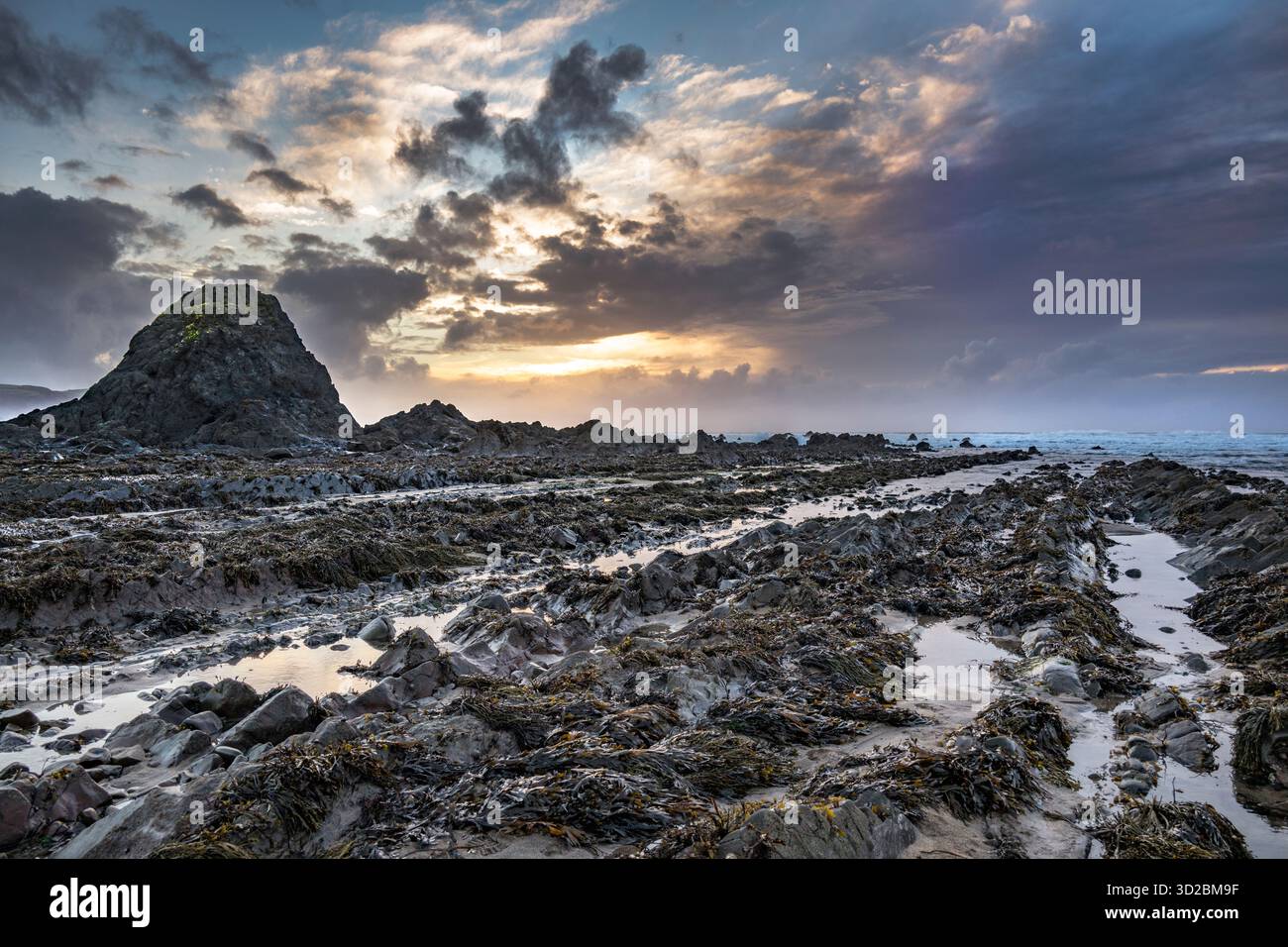 Sun sets behind Black Rock on Widemouth Bay beach Cornwall Stock Photo