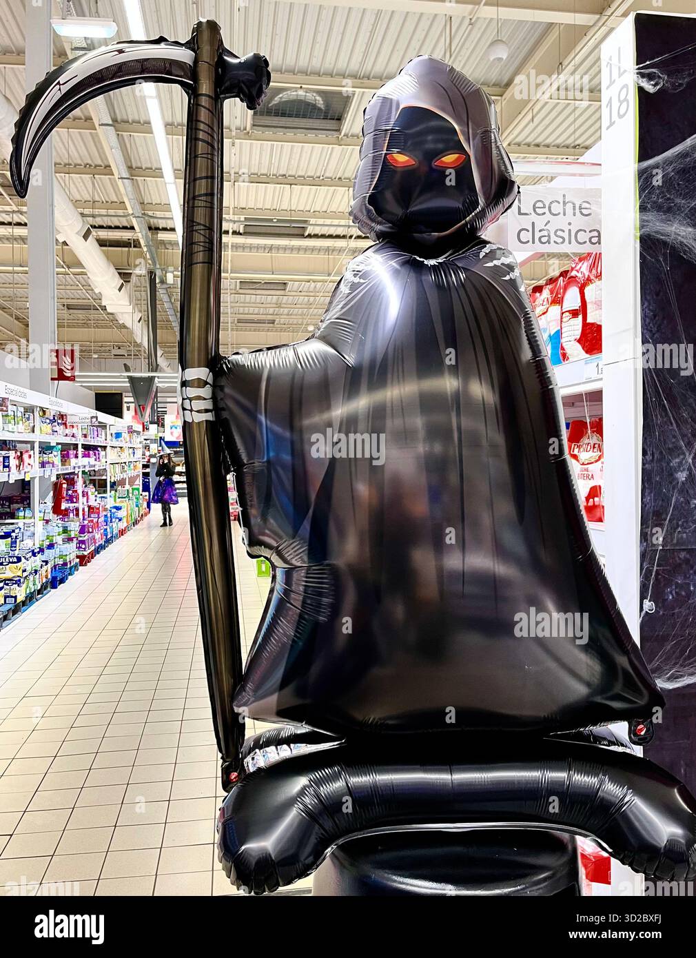 Inflatable grim reaper inside a Carrefour Hypermarket with a shop attendant in a witch uniform behind on halloween Santander Cantabria Spain Europe - Smartphone Captured Stock Image
