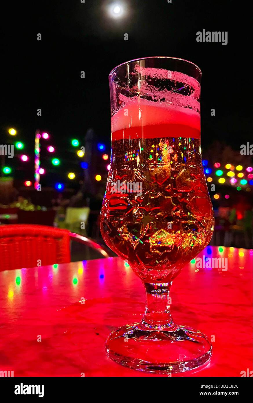 Half full glass of lager on an outside terrace table lit by coloured decorative lights and a half moon on halloween Santander Cantabria Spain Europe - Smartphone Captured Stock Image