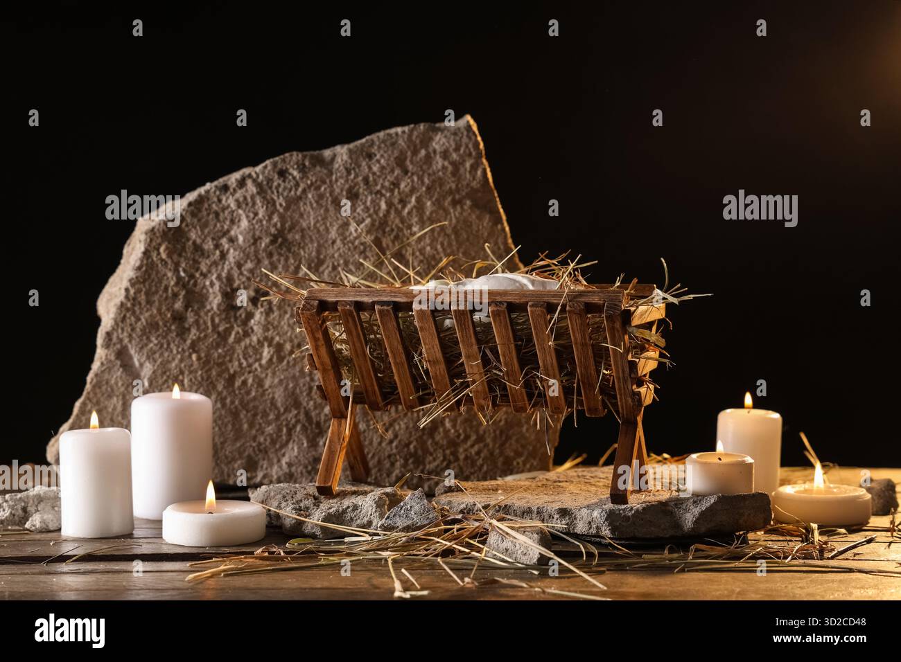 Manger with baby Jesus, rocks and burning candles on table against dark ...