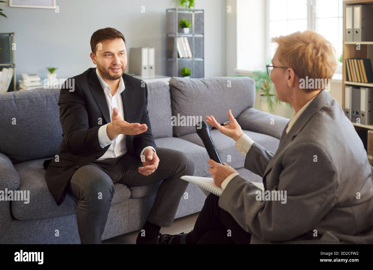 Businessman speaking in interview on sofa, interviewer with microphone in office Stock Photo