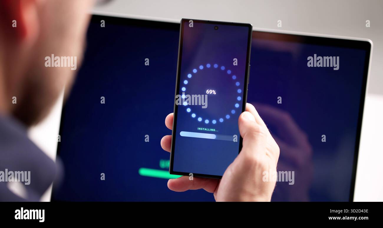 Man At Workplace Installing Software Update Progress On Smart Phone. Male Engineer Loading Patch From Internet Stock Photo