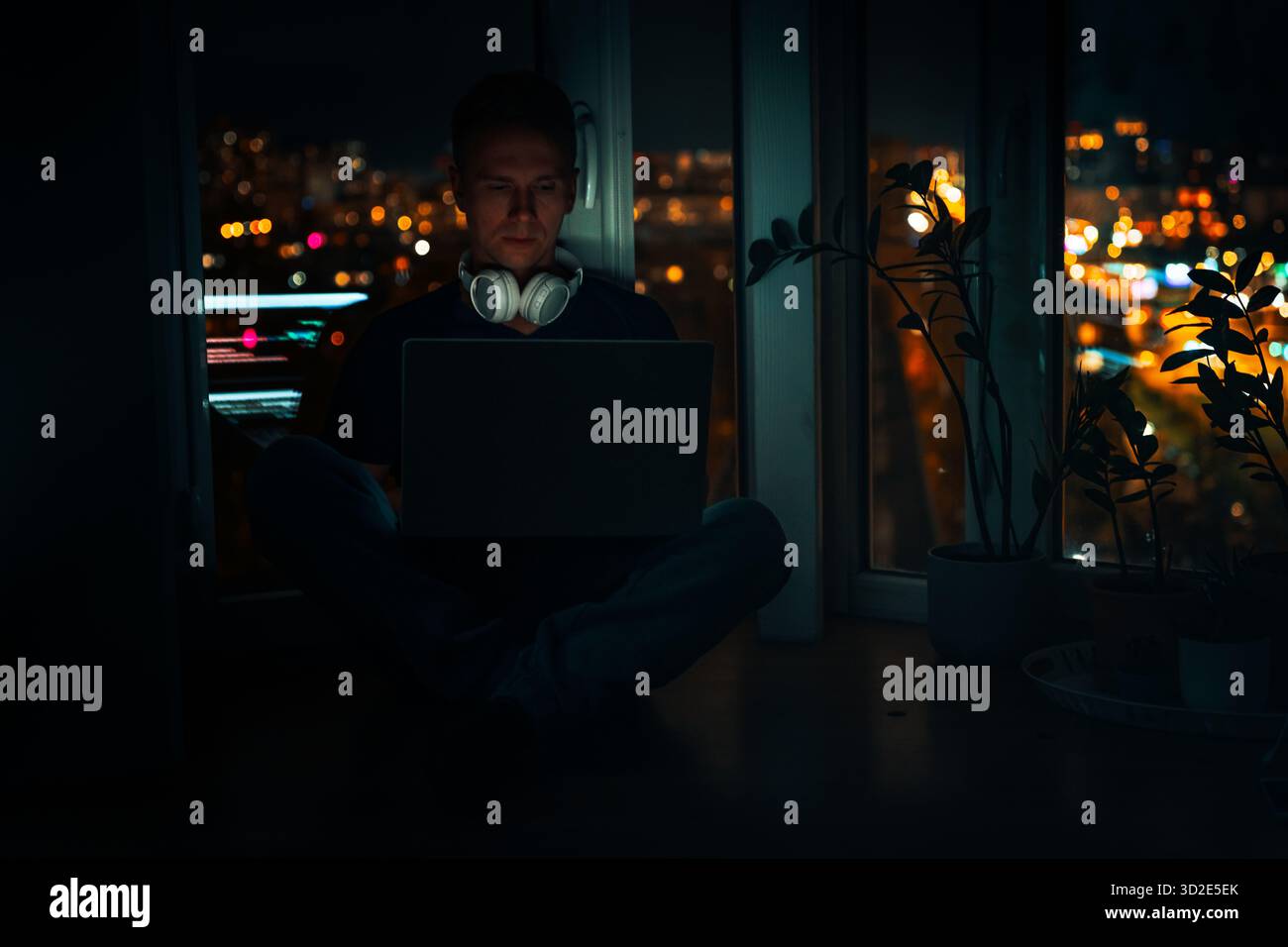 A young male developer is programming a code script late at night with beautiful city lights at night. Stock Photo
