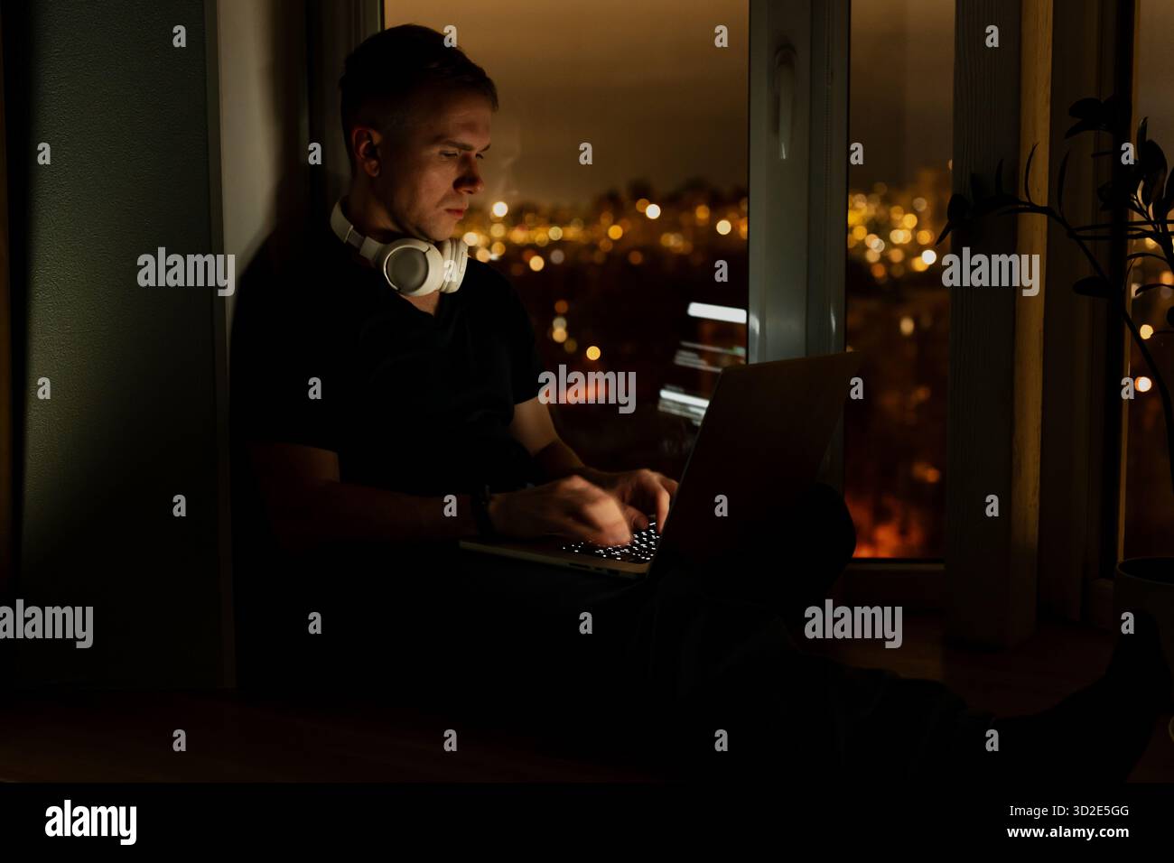 A young male developer is programming a code script late at night with beautiful city lights at night. Stock Photo