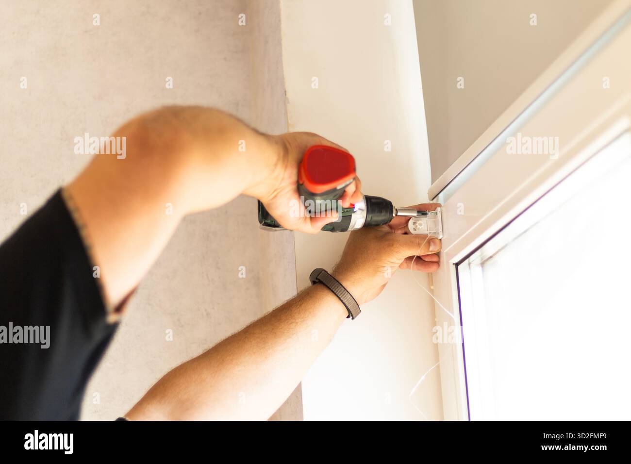 Man using screwdriver to attach roller blind mechanism to window during installation. Stock Photo