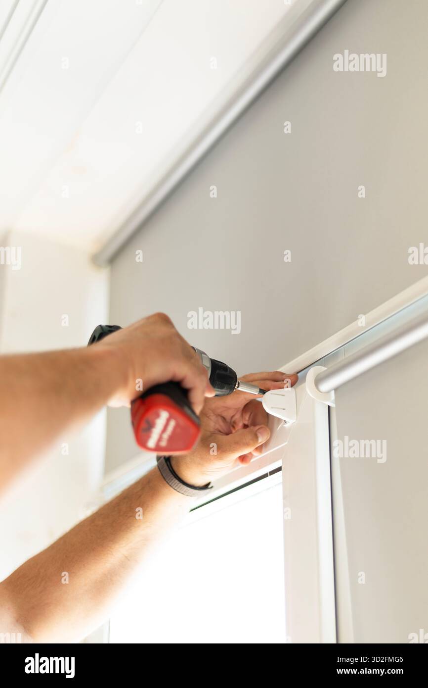 Male hands holding screwdriver while installing foil roller blinds on window frame. Stock Photo