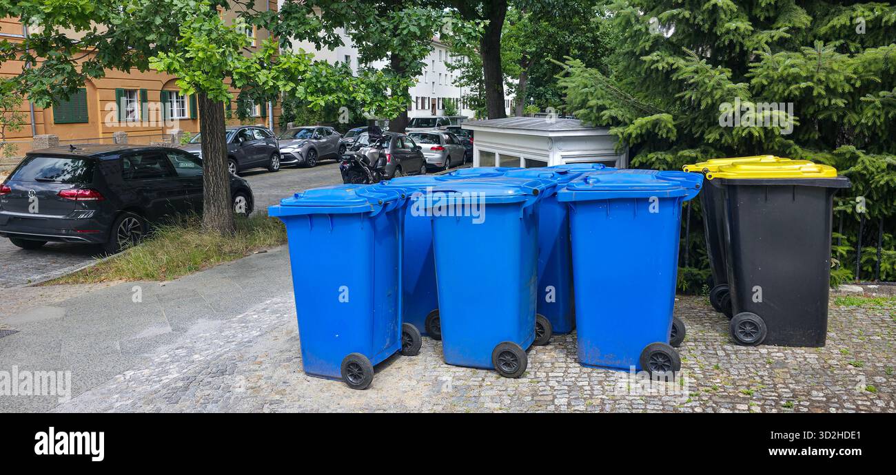 Berlin, Germany - July 03, 2025: . Colorful waste bins are positioned along the street with parked cars and lush greenery nearby - Smartphone Captured Stock Image