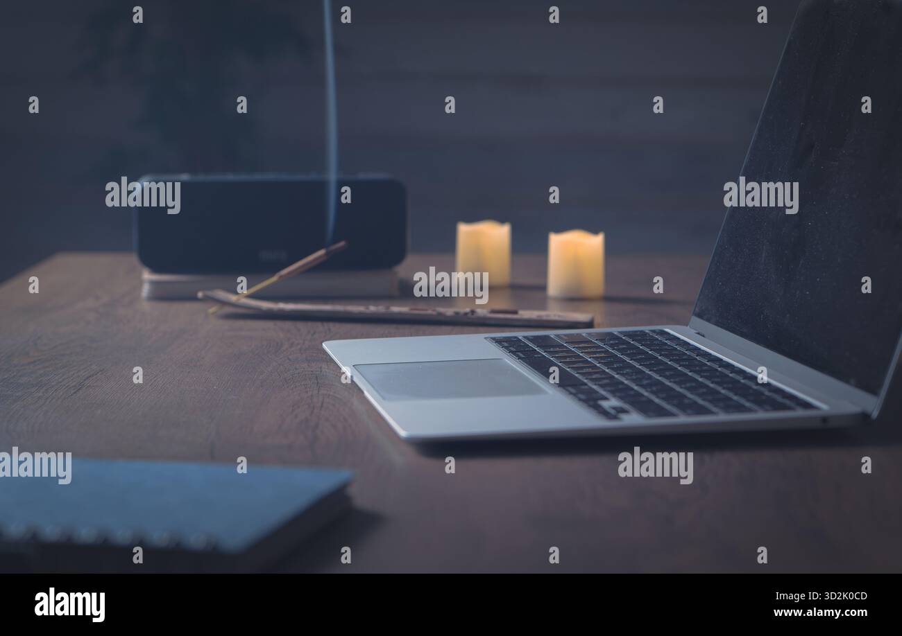 Mindful working. Serene home office table — desktop computer, aroma stick smoke, soft lamp light and gentle sound flow create creative focus Stock Photo