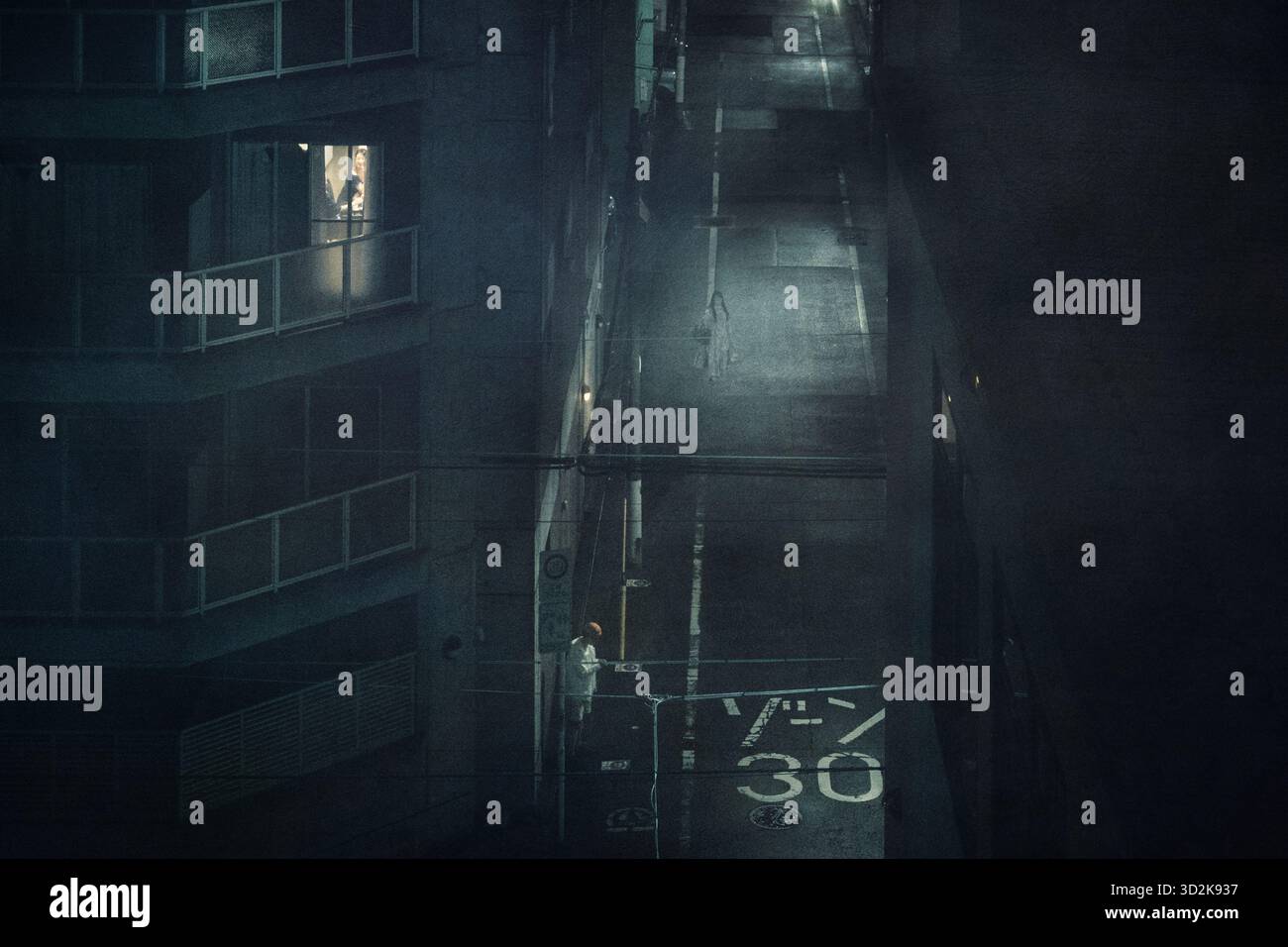 A backstreet in Shinjuku, Tokyo at night, with three people visable in atmospheric street lighting - Stock Image