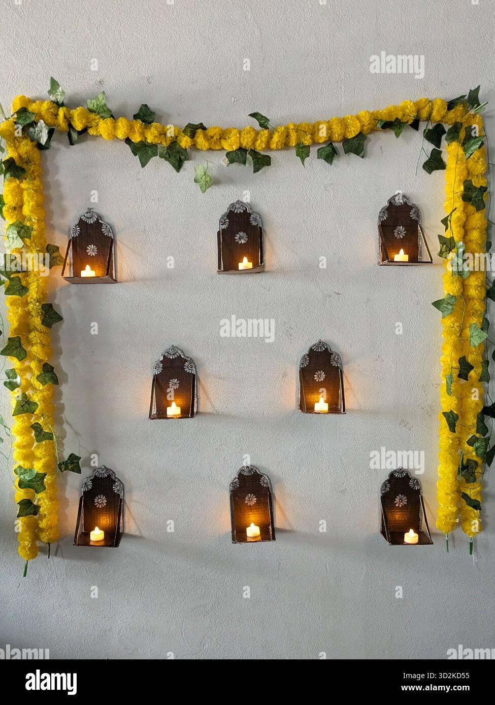 The warm, golden glow of the lit candles or tea lights stands out against the dark metal and the light wall. - Smartphone Captured Stock Image