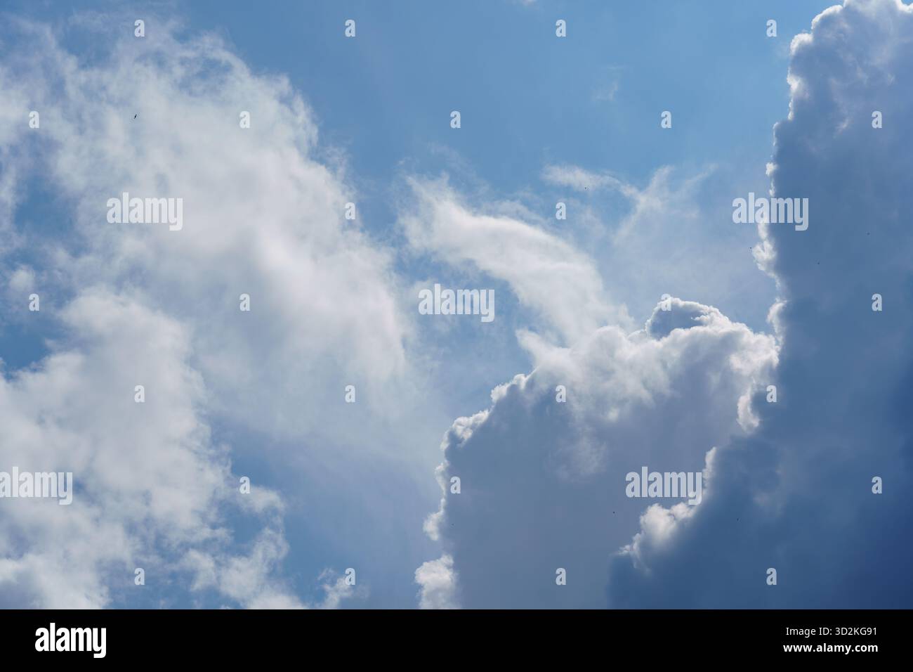Soft, fluffy clouds float in a clear blue sky, creating a peaceful atmosphere on a warm sunny day. Stock Photo