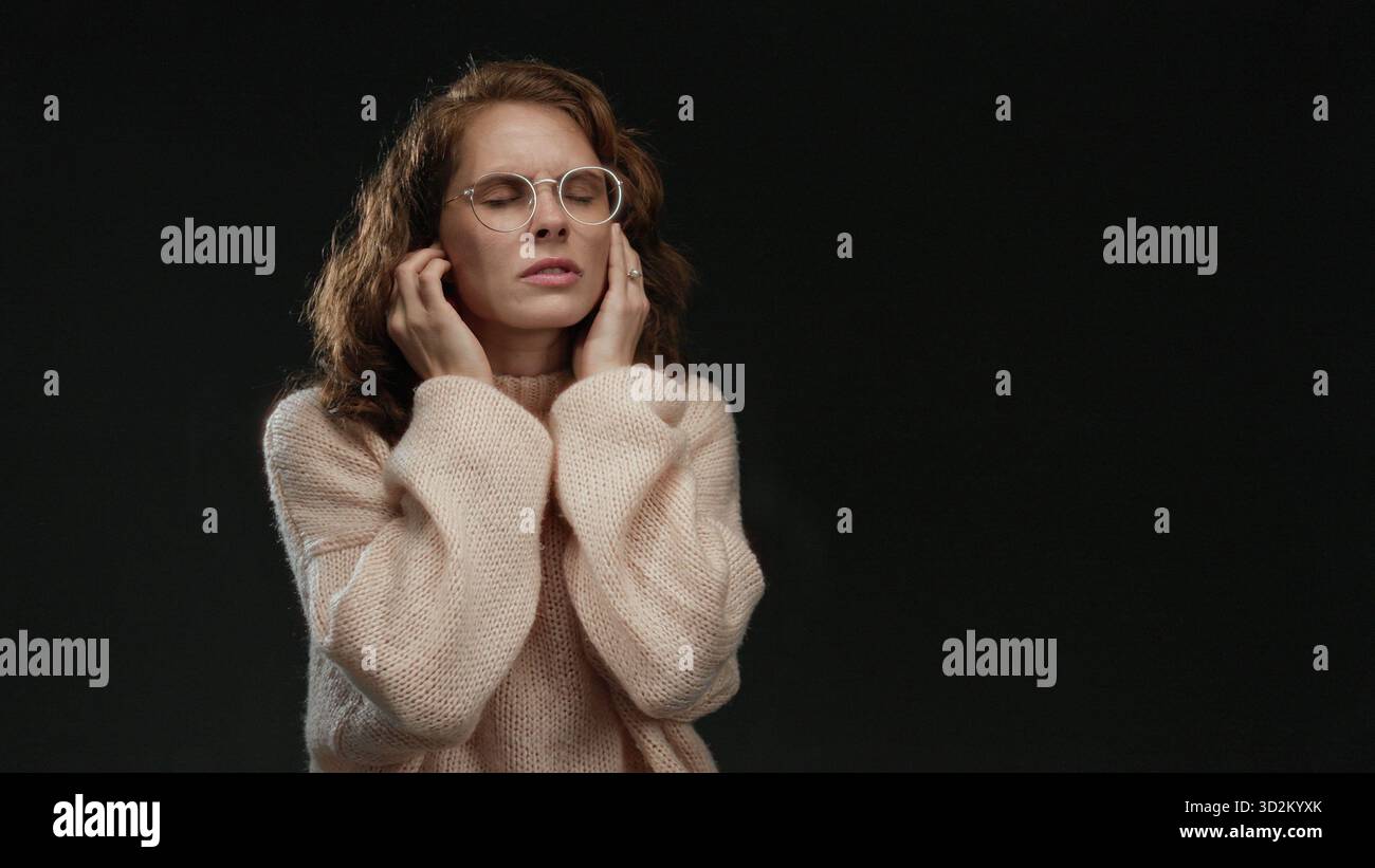 Woman covers her ears to block noise on isolated black background ...