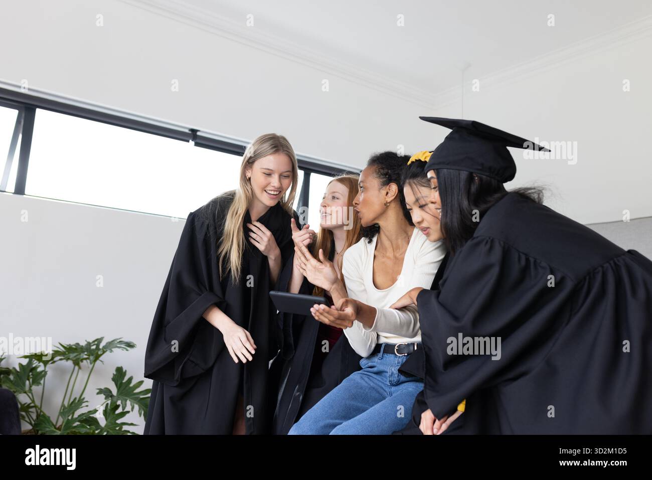 Graduating students in caps and gowns sharing joyful moments on smartphone. Graduation, celebration, academic, achievement, technology, communication || Model released Stock Photo