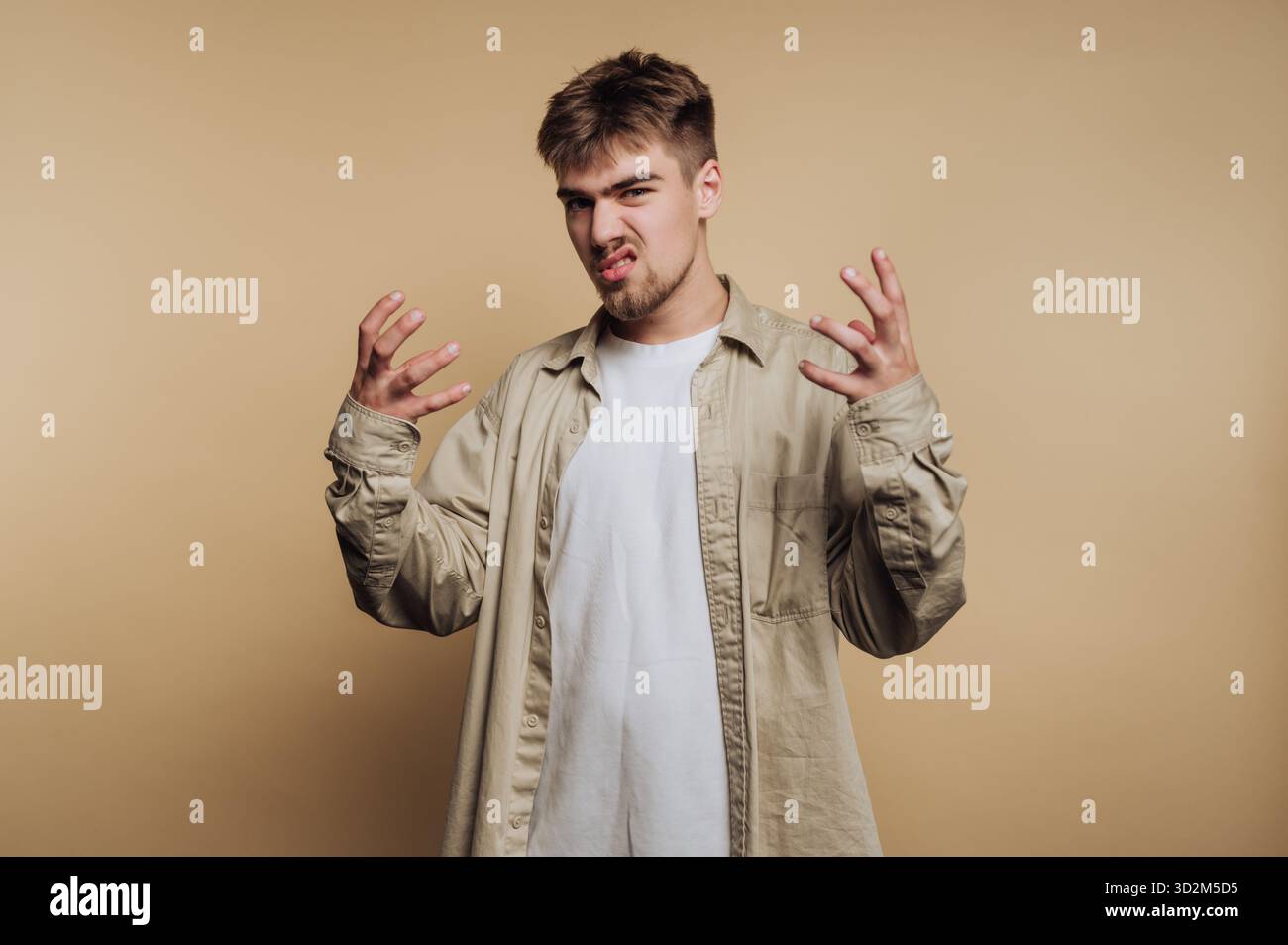 Young man expressing frustration with hands raised against beige background. Stock Photo