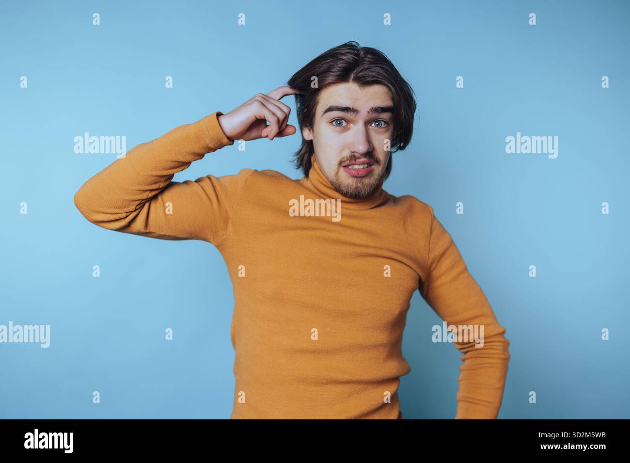 Young man in orange sweater looking confused against blue background. Stock Photo