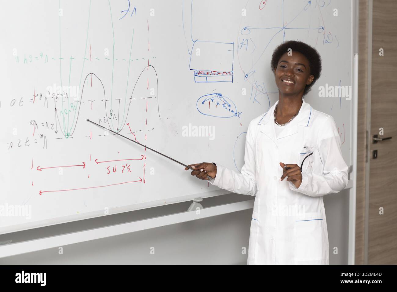 African American smiling woman math teacher stands at black board with pointer Stock Photo
