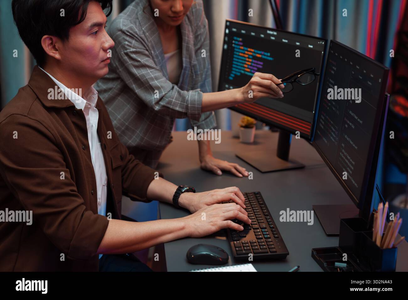 IT developers discussing with point to intelligent website development coder system running data online two screens information technology at neon lig Stock Photo