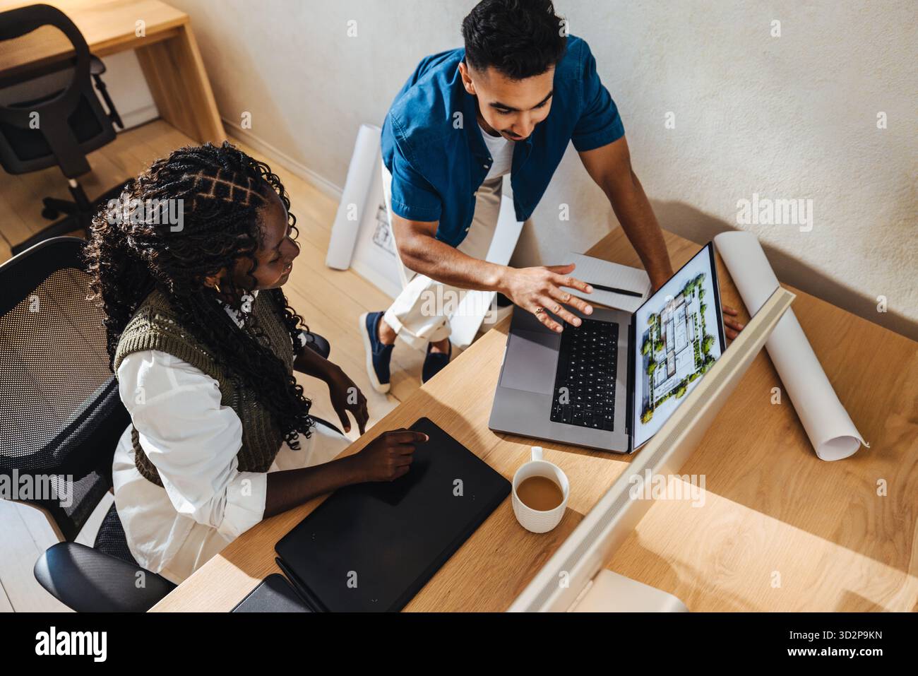 Two young professionals working together on a laptop, discussing architectural designs in a modern, collaborative workspace. Stock Photo
