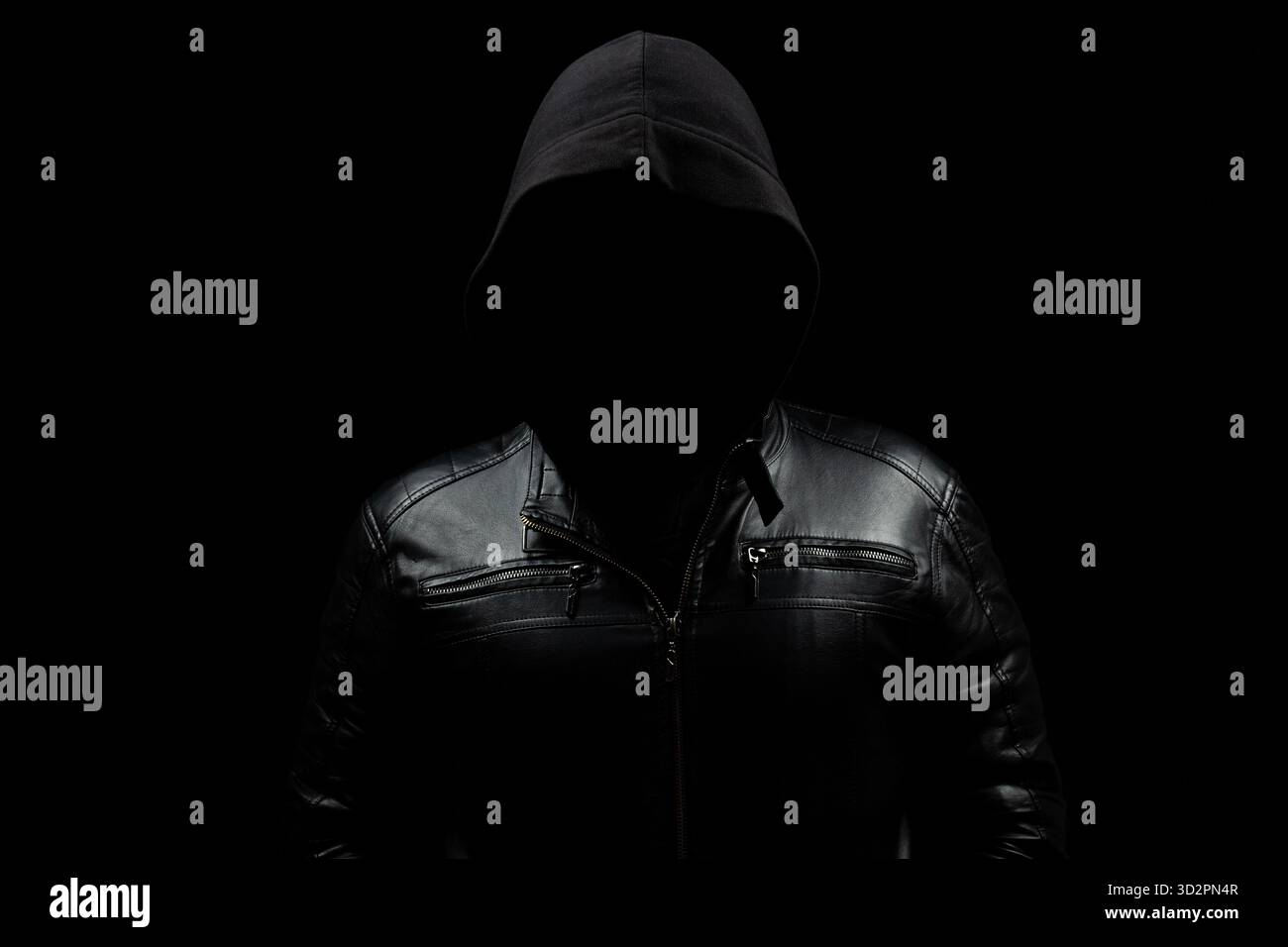 Close up to a faceless hooded hacker man in the shadows wearing a leather jacket and a black background Stock Photo
