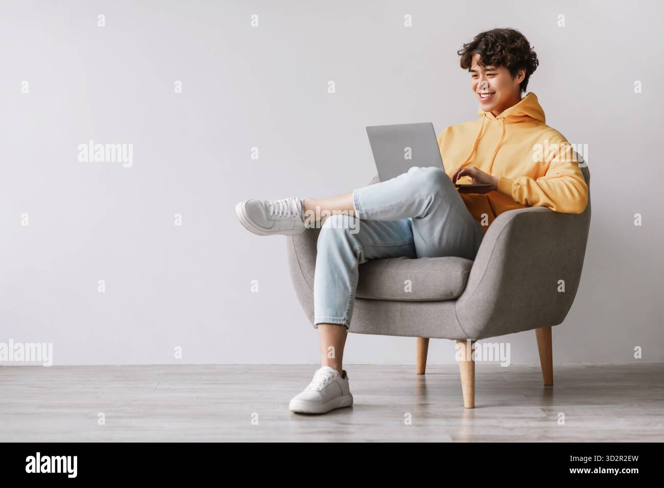Young Asian Man Enjoys Remote Work While Sitting Comfortably in an Armchair Stock Photo