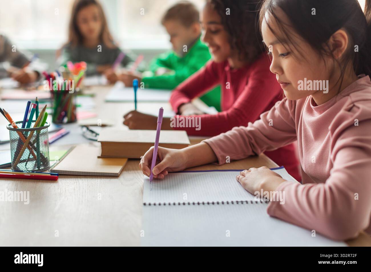 Korean Schoolgirl Taking Notes While Learning With Classmates in Modern Classroom Setting Stock Photo