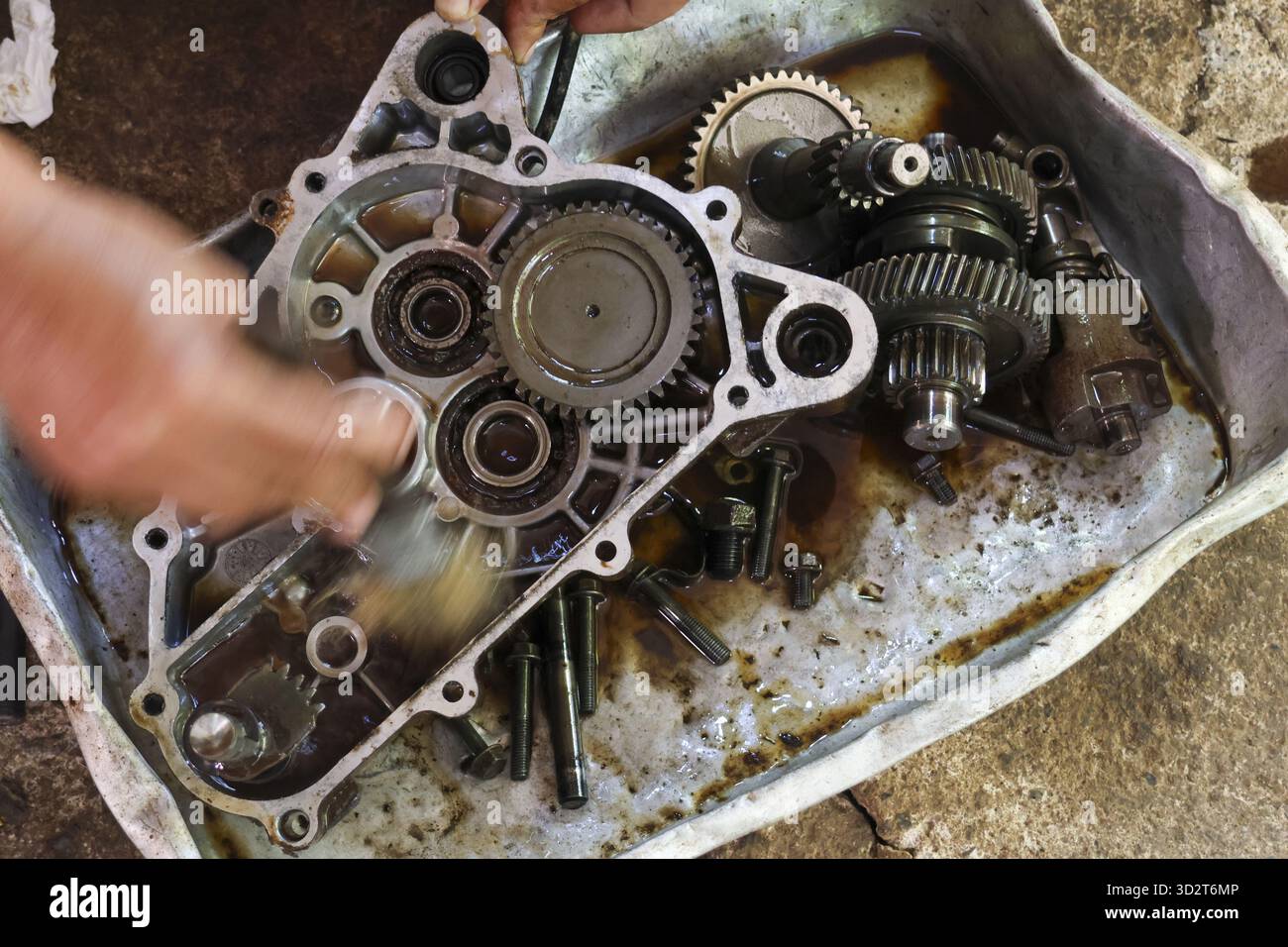 Skilled mechanic performing complex gearbox repair and engine maintenance. intricate assembly of gear and transmission parts in an oily motorcycle wor Stock Photo