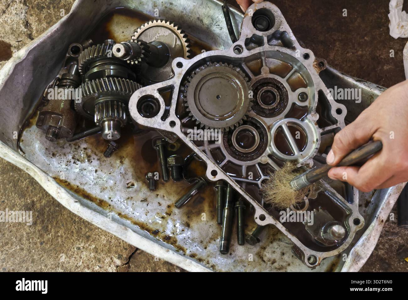 Meticulous mechanic cleaning dirty transmission gearbox case with brush. Close up view of human hand working on oily metal engine part during auto rep Stock Photo