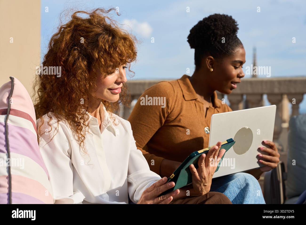 Diverse women collaborating on technology device outdoors Stock Photo